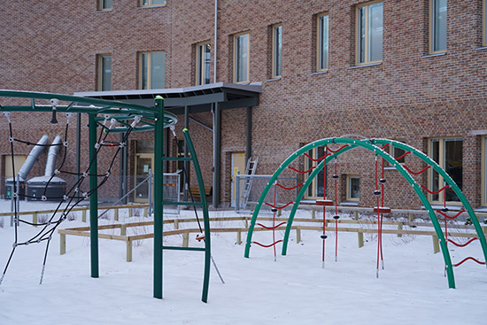 Gröna klätterställningar på skolgården framför Hemlingborgs förskola. Tegelfasaden syns bakom.