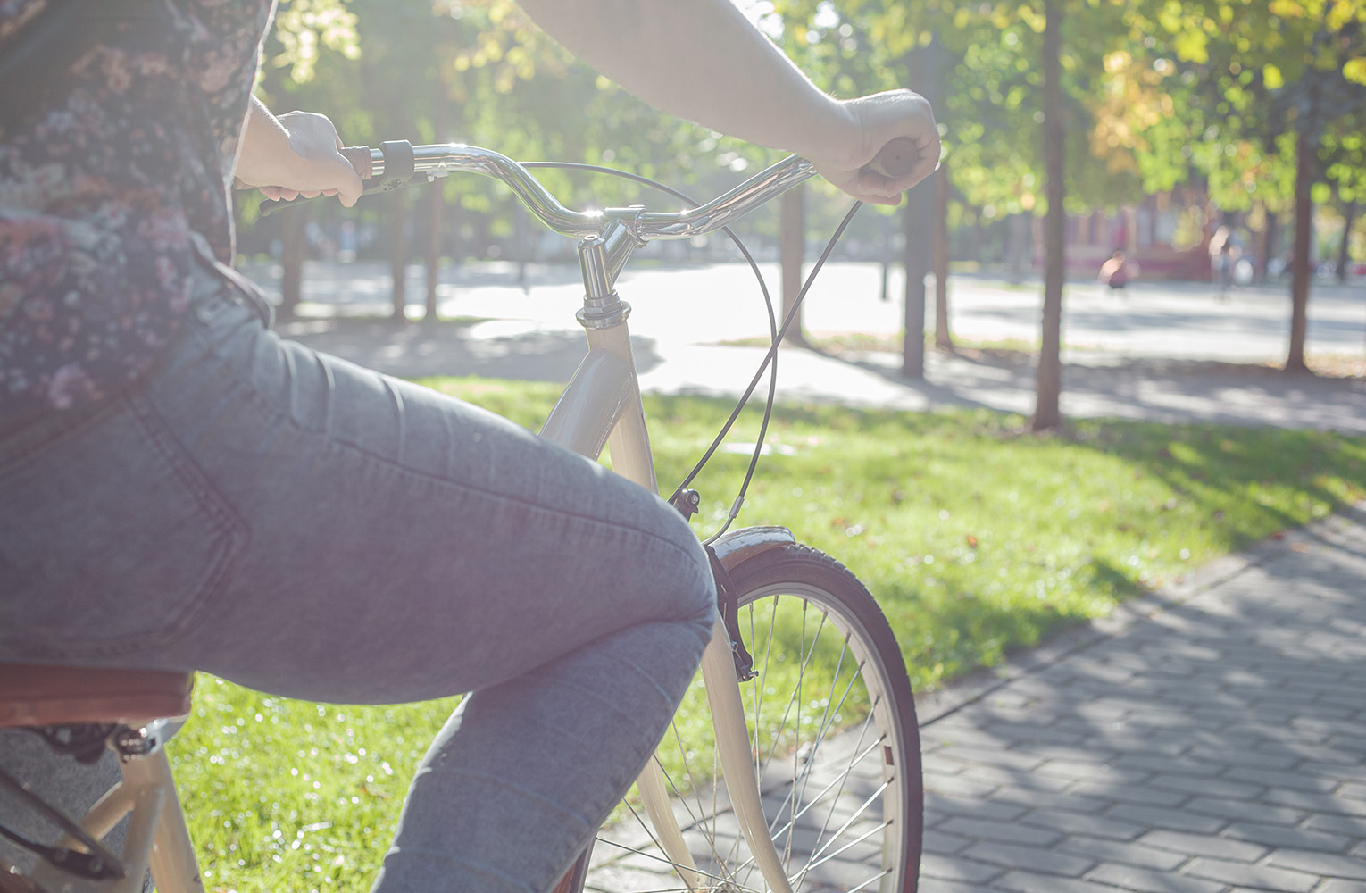 Person i jeans cyklar på en beige cykel i en grönskande park.